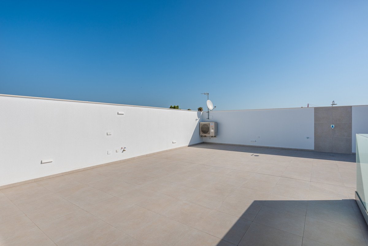 A spacious, tiled rooftop terrace with white walls, an air conditioning unit, and a satellite dish under a clear blue sky.