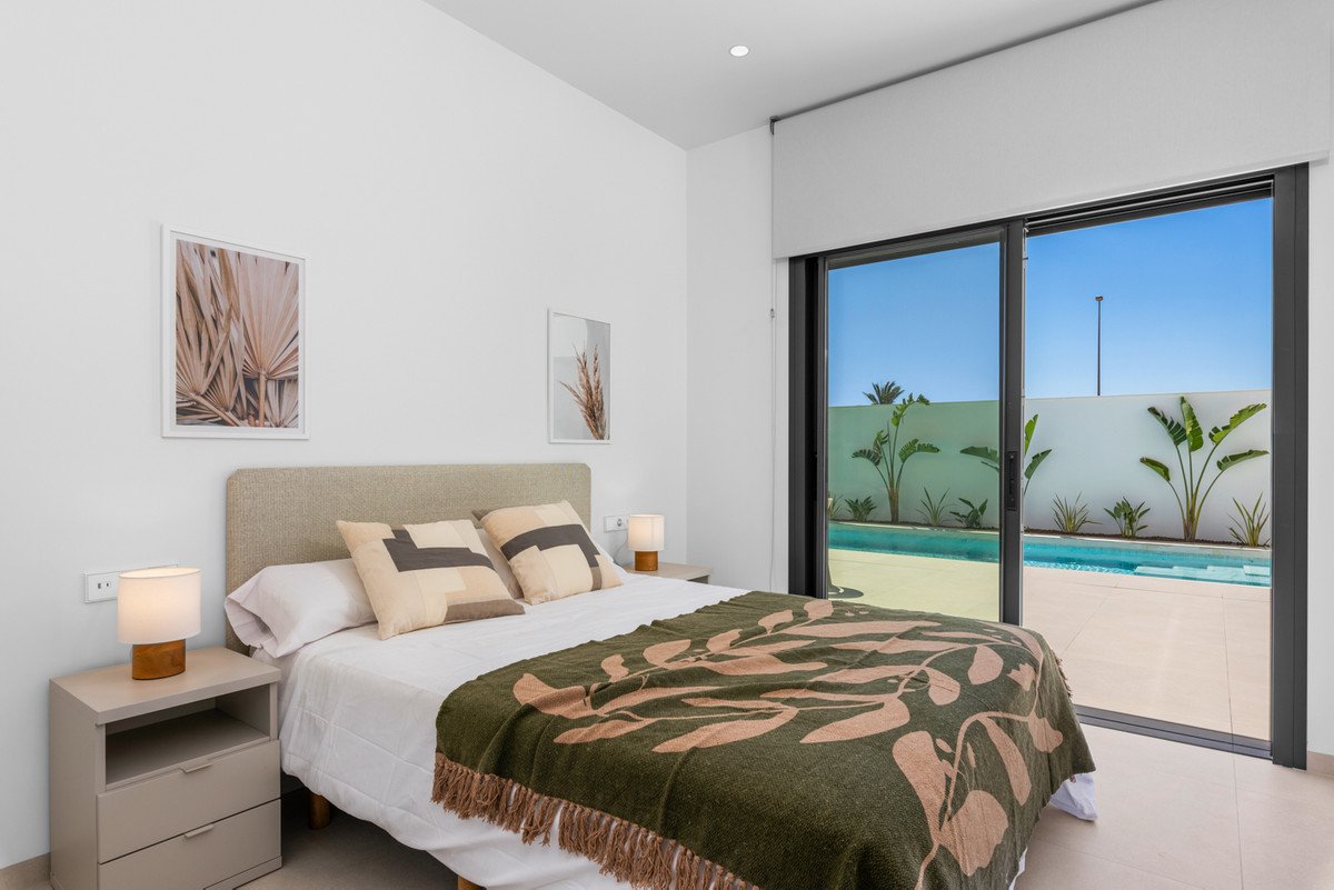 A modern bedroom with a bed, nightstands, and a large sliding door opening to a private swimming pool and tropical garden.