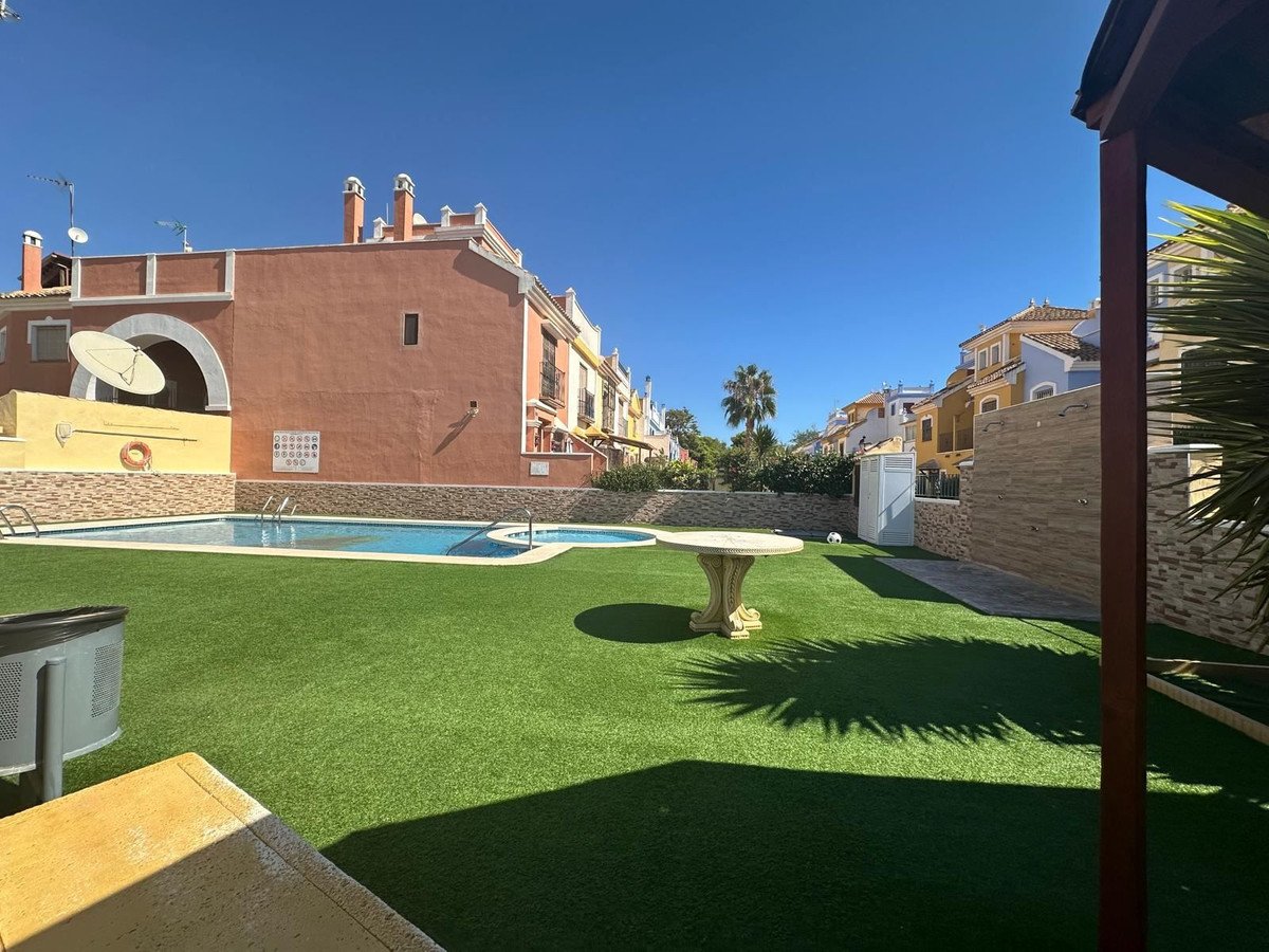 Communal pool and garden area with artificial grass, surrounded by townhouses on a sunny day.