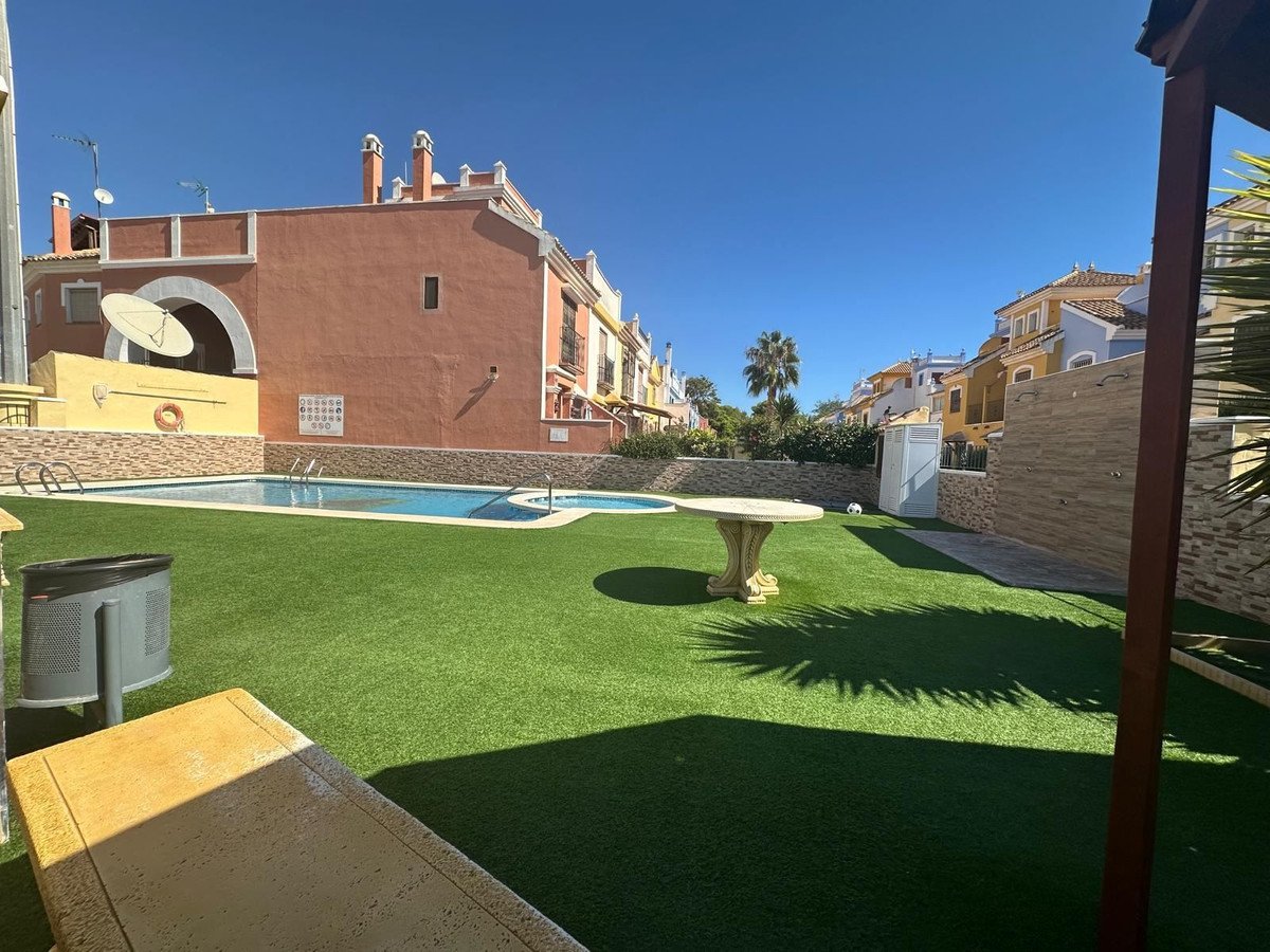 A sunny courtyard with a swimming pool, artificial turf lawn, and a table, surrounded by residential buildings.