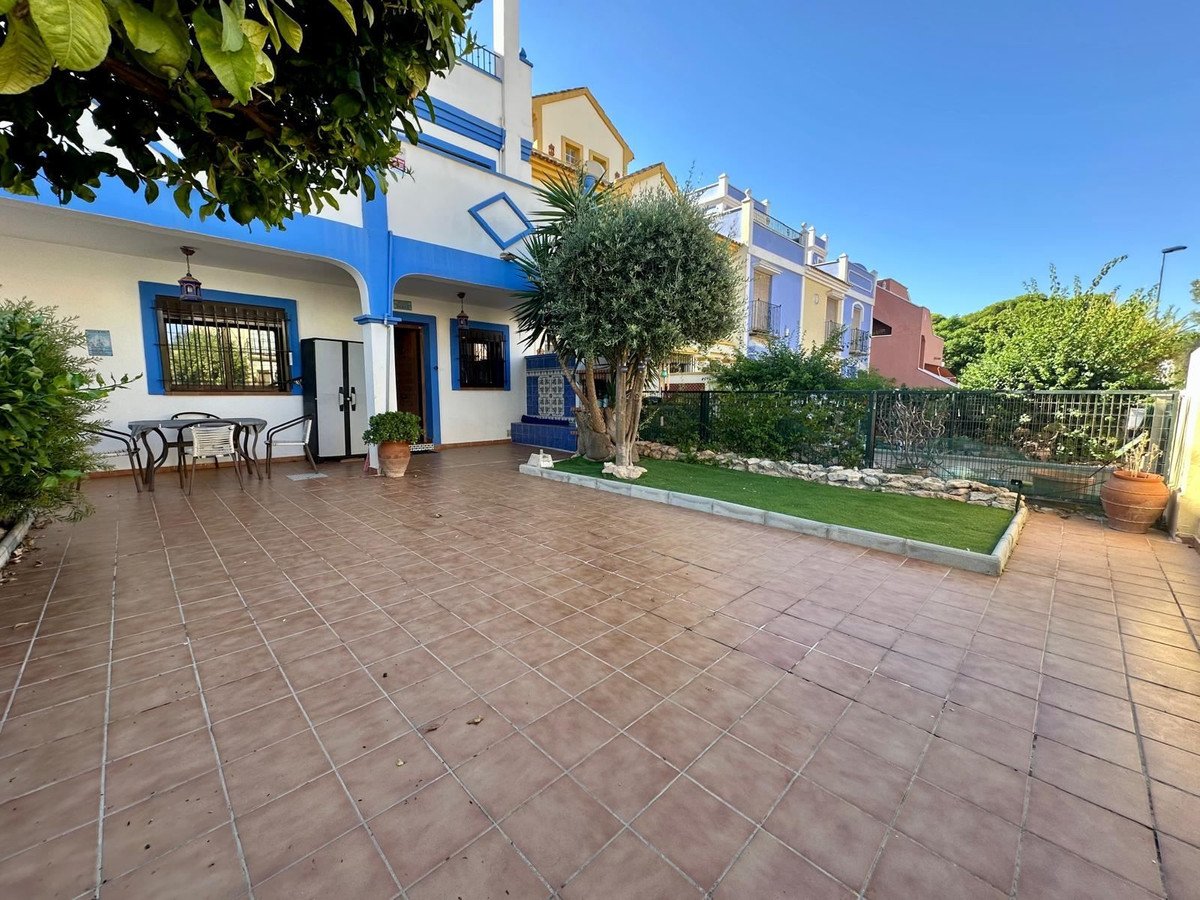 Tiled terrace with garden, a small tree, and colorful houses in the background under a clear blue sky.