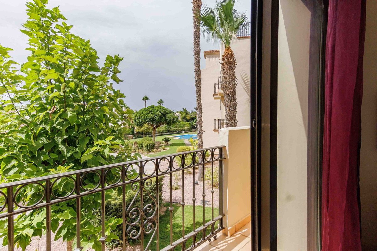View from a balcony overlooking a garden with a swimming pool, palm trees, and lush greenery.