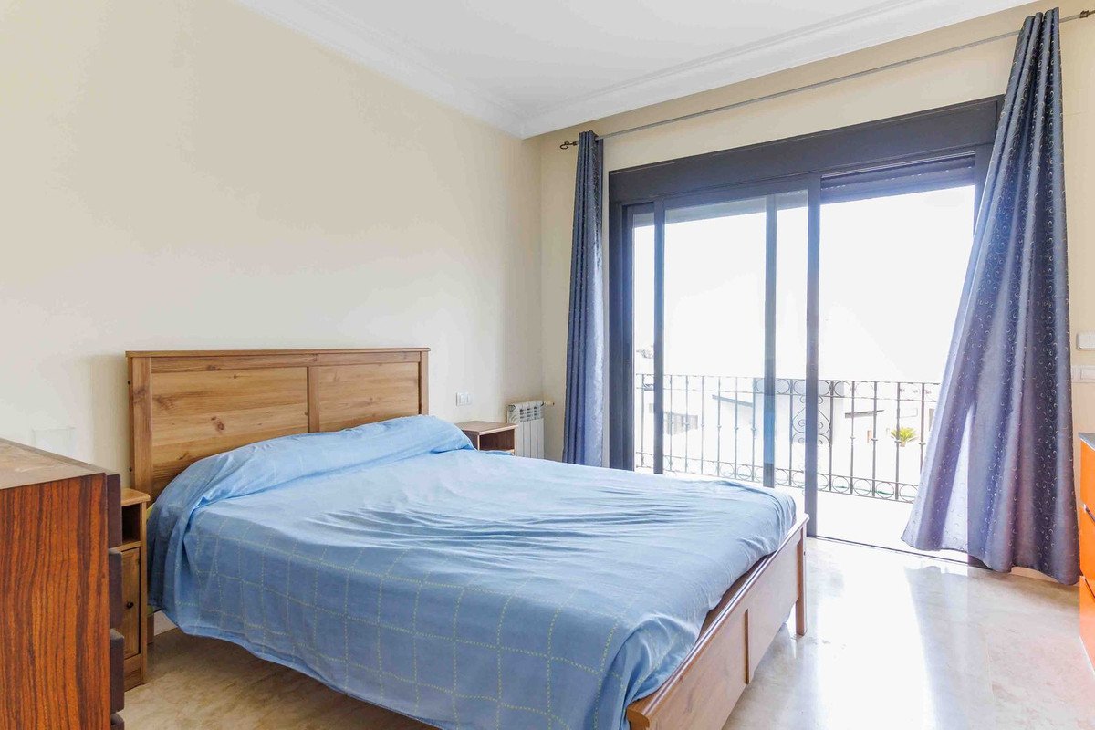 Bedroom with a large wooden bed, blue linens, and a sliding glass door leading to a balcony with a view.