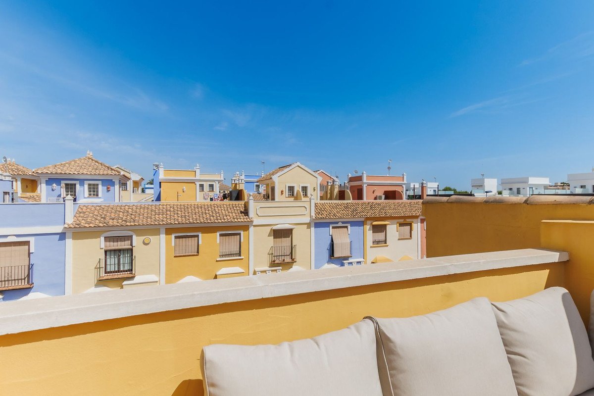 View from a terrace with cushioned seating, overlooking colorful houses under a clear blue sky.