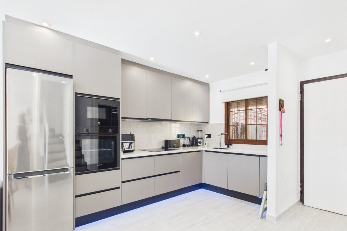 Modern grey kitchen featuring stainless steel refrigerator, built-in oven, microwave, and sleek cabinetry with under-cabinet lighting.