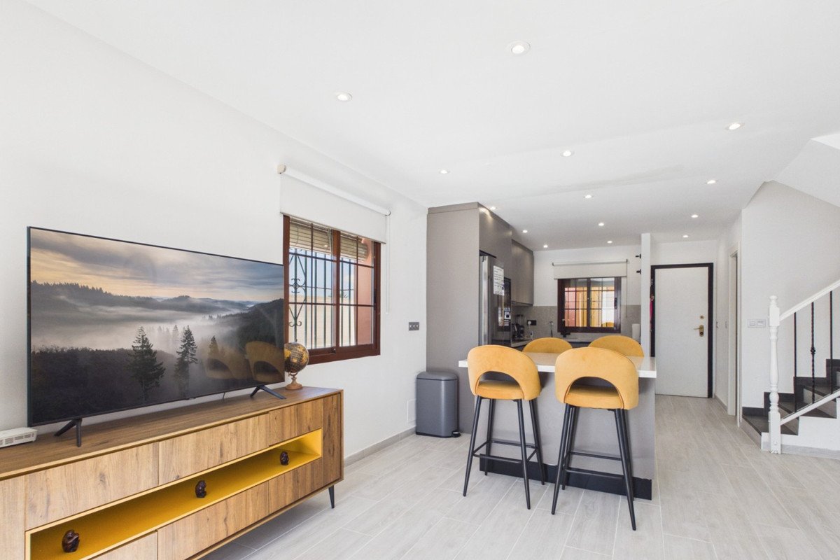 Modern open-plan living and kitchen area with a TV, island with bar stools, and a staircase.
