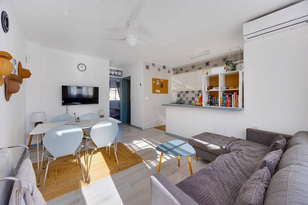 Bright living and dining area with a kitchenette, featuring a sofa, dining table, and TV.
