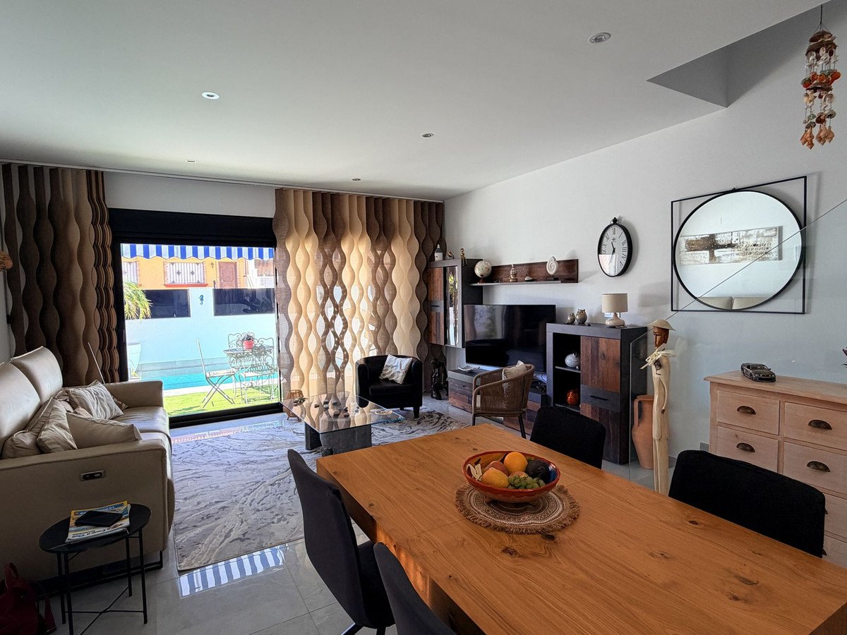 Modern living and dining room with a sofa, dining table, and a view of the outdoor pool and garden area.