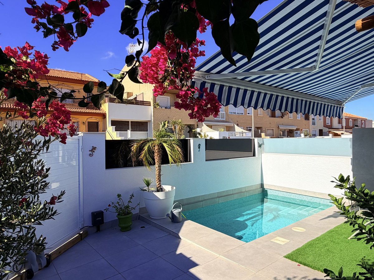 A private patio with a small swimming pool, artificial turf, blooming flowers, and a striped retractable awning.