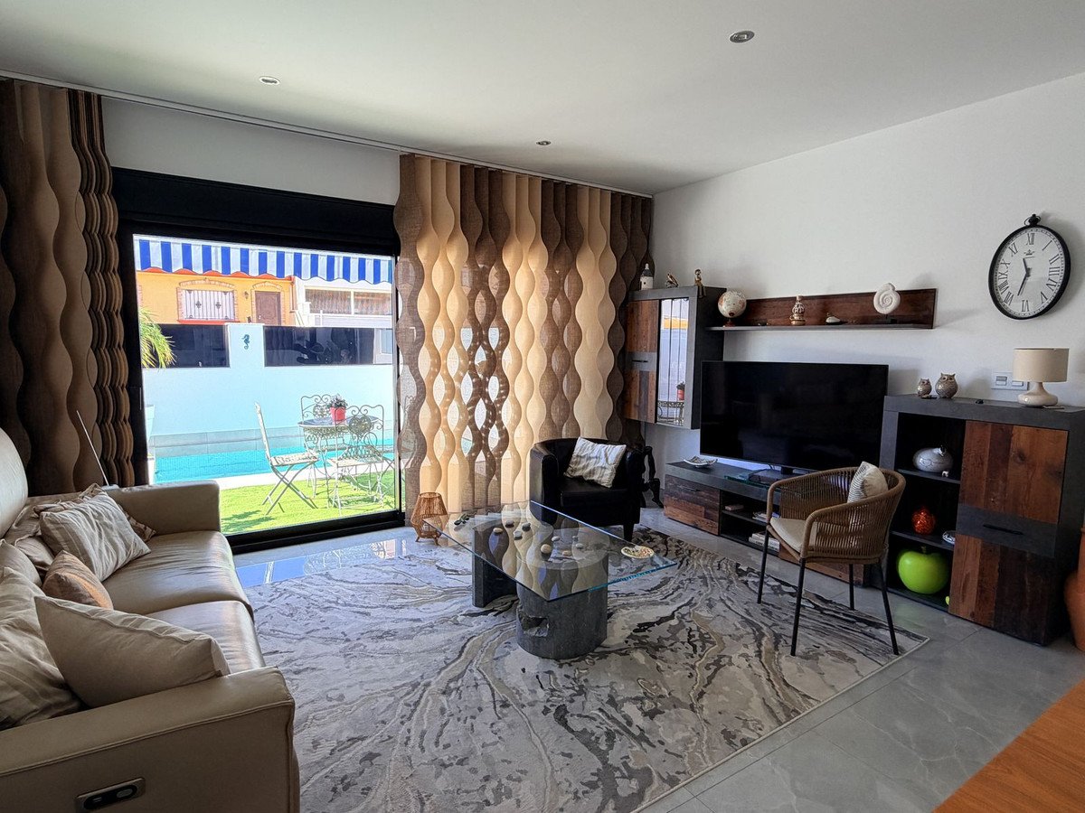 Modern living room with comfortable sofa and chairs, featuring a large window with a view of the outdoor pool and garden.