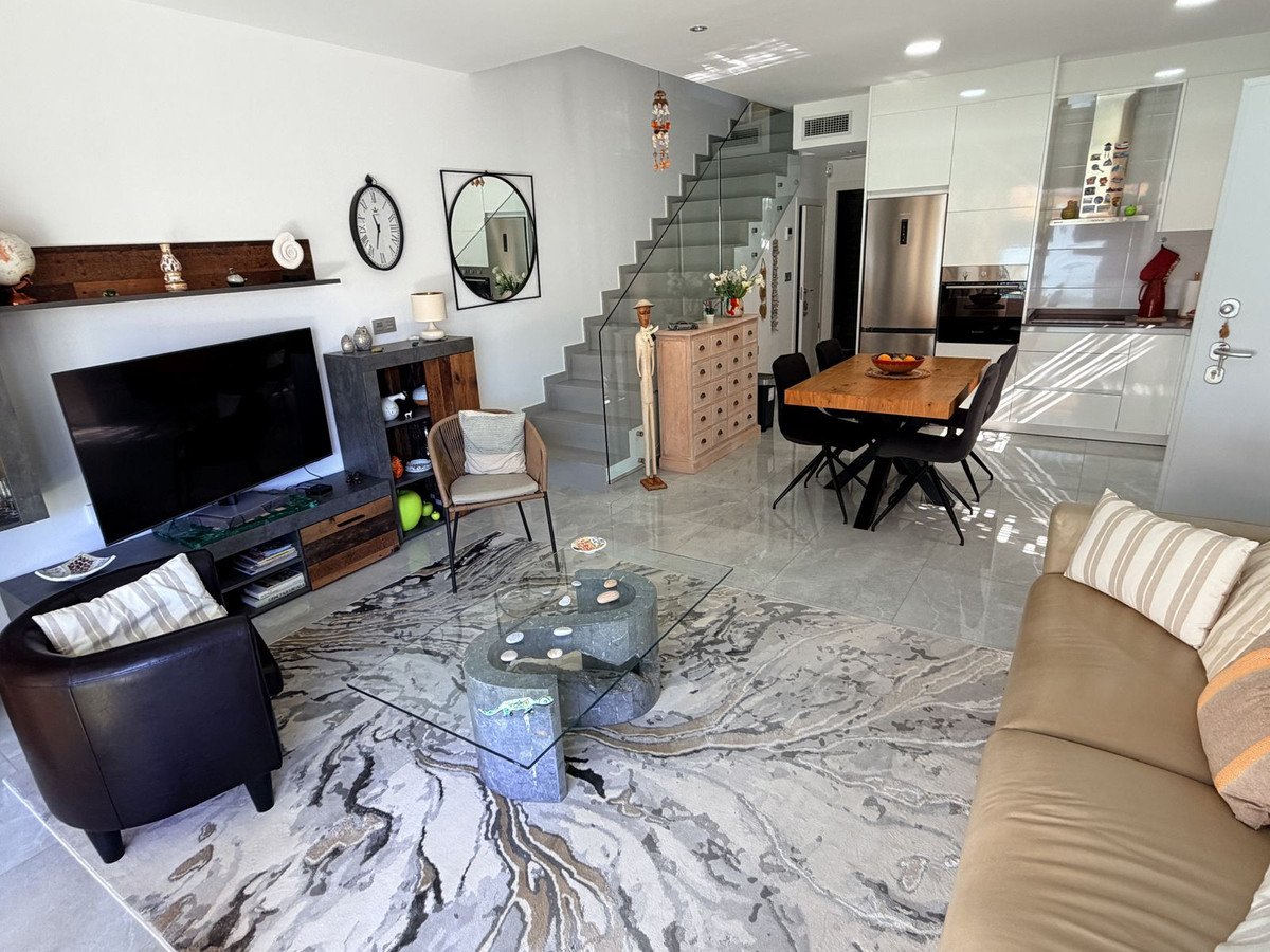 Modern living, dining, and kitchen area with stylish furniture, a wooden dining table, and sleek white cabinets.