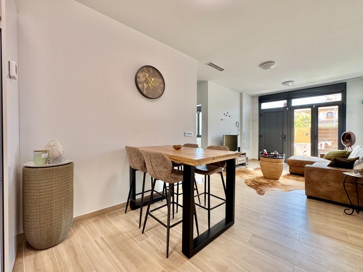 A modern dining area with a high table and stools, adjacent to a living room with a sofa and large windows.