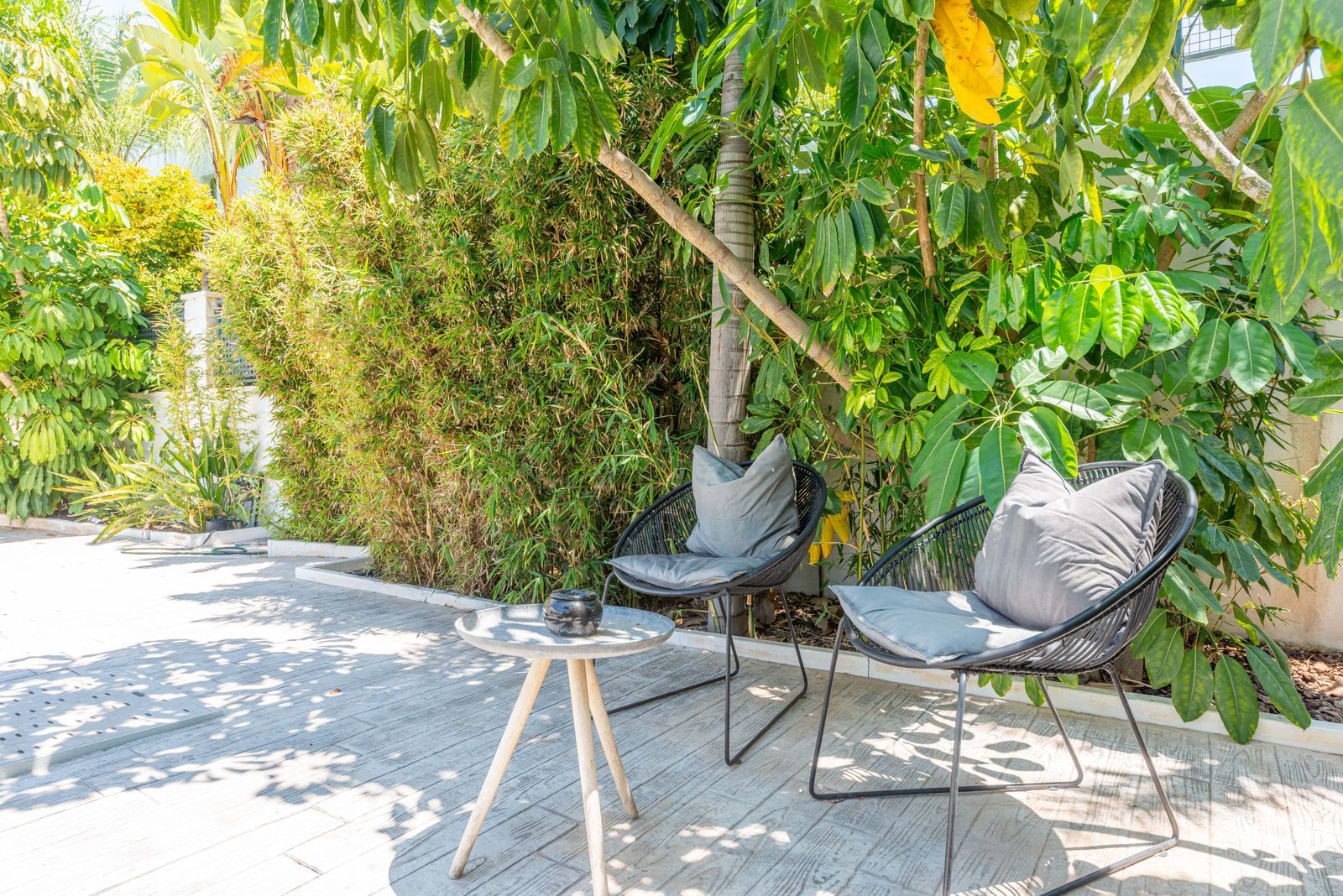 Buitenzitje met stoelen en een tafeltje, omgeven door weelderige tuin.