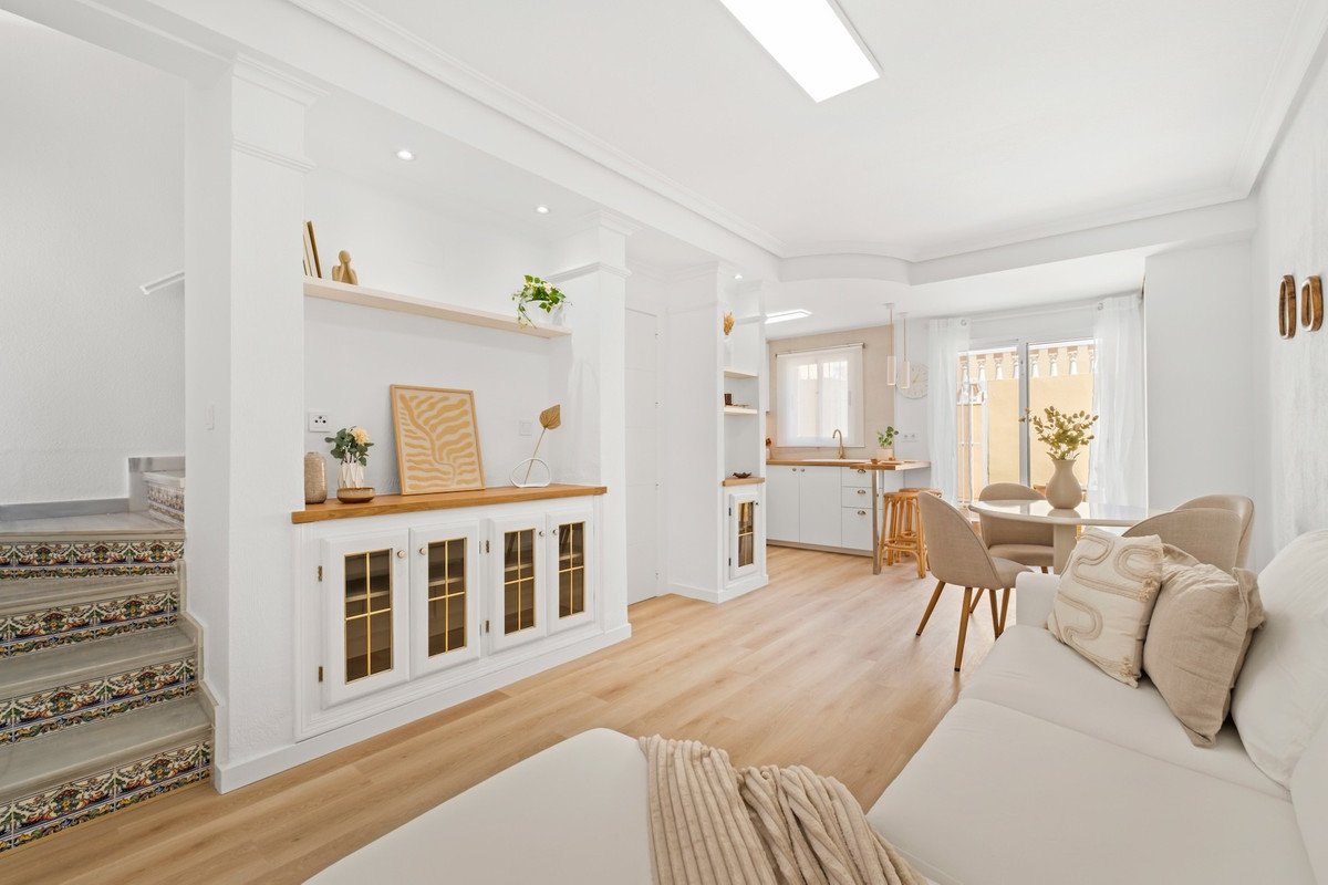 Bright open-concept living, dining, and kitchen area with white walls, light wood floors, and stylish furniture.