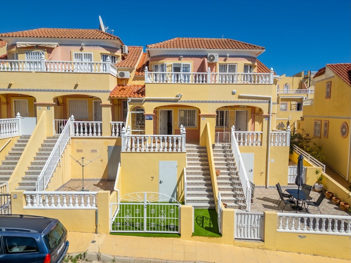 Yellow townhouse with multiple levels, balconies, outdoor seating area with a table and chairs, and a small green lawn.
