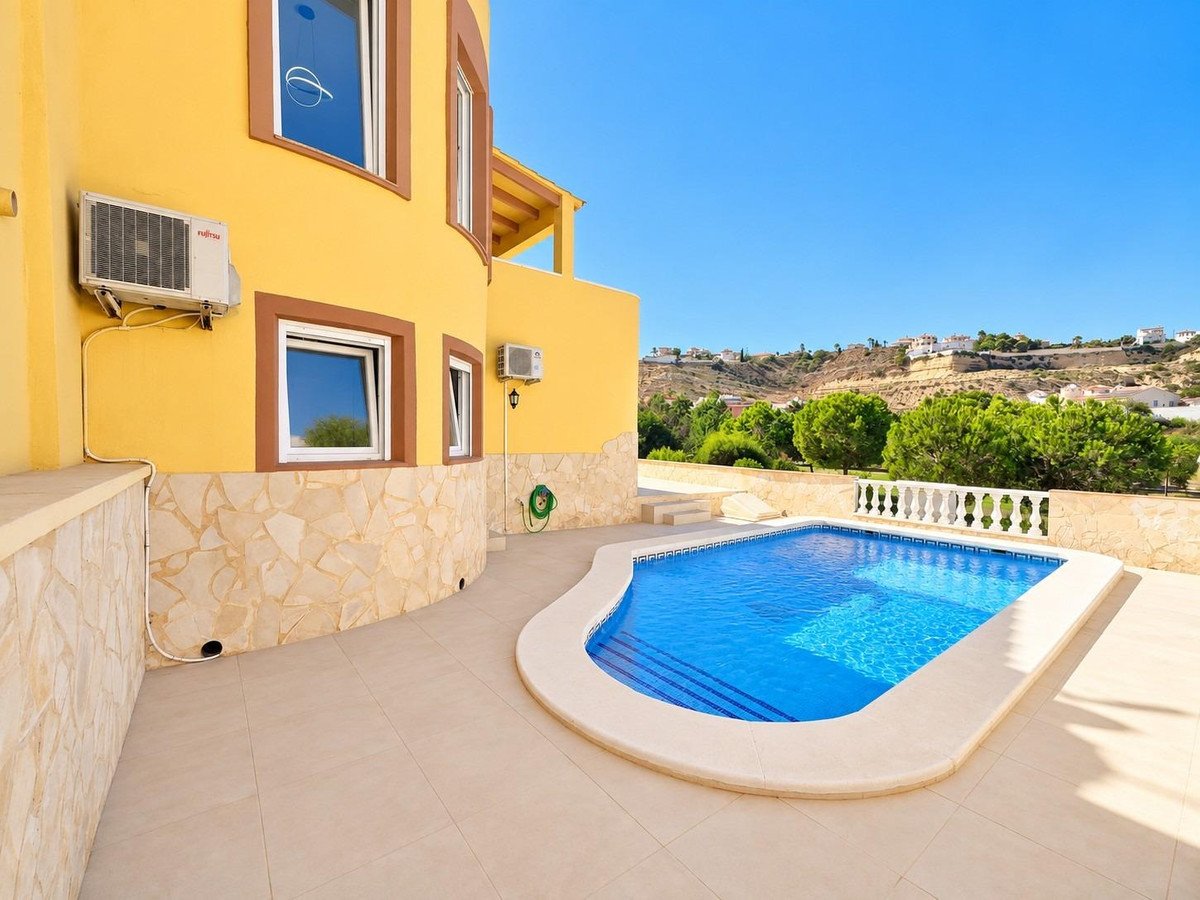 Exterior view of a yellow villa with a private pool and a scenic view of rolling hills.