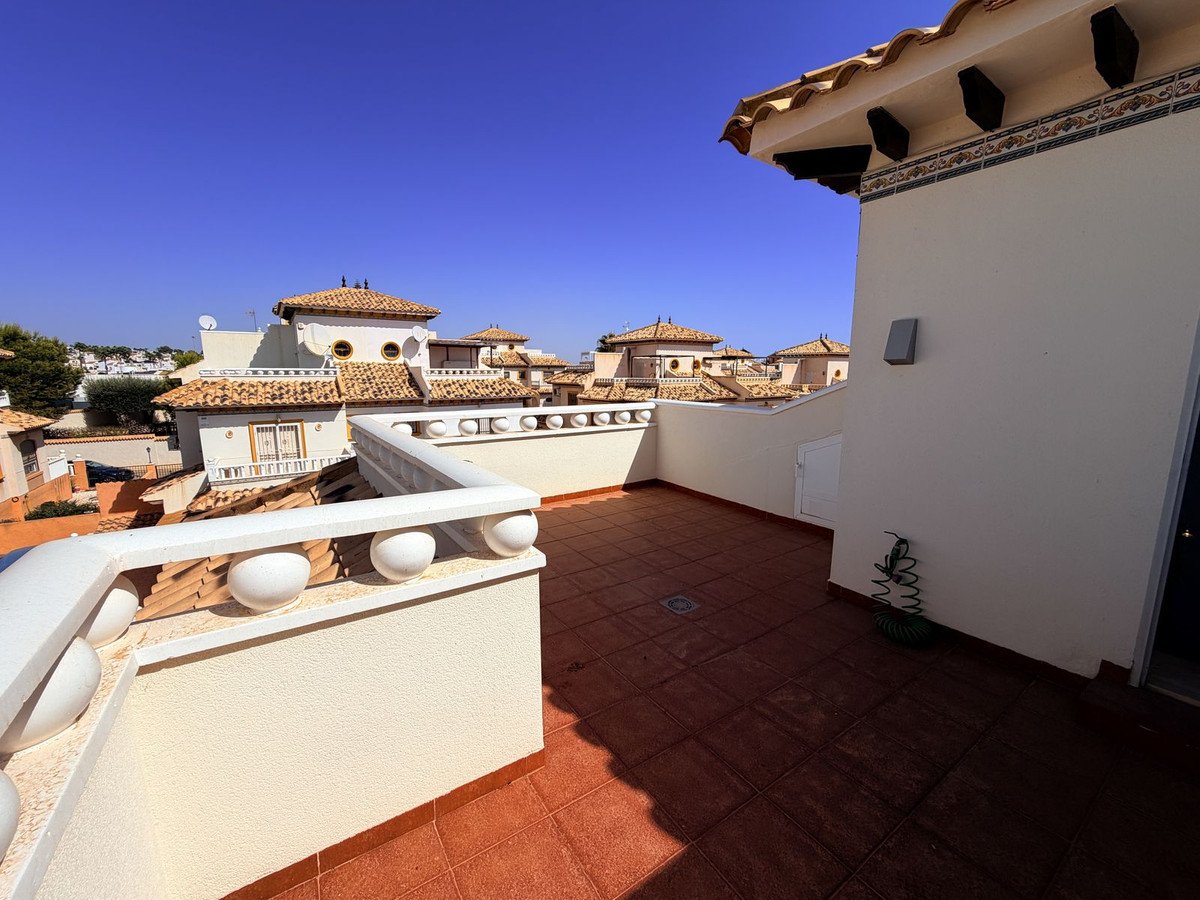 Spacious terrace with terracotta tiles and white balustrade overlooking Mediterranean-style buildings under a clear blue sky.