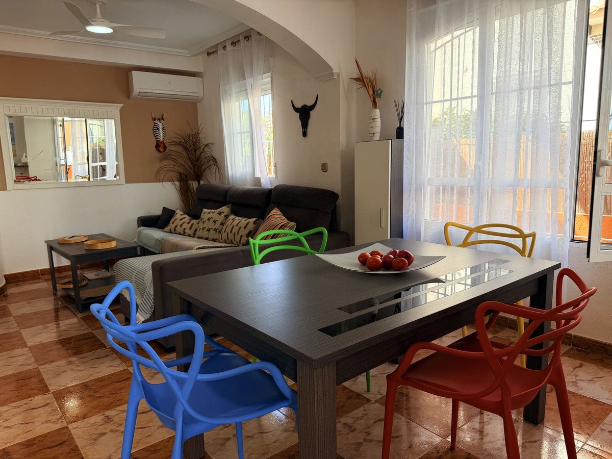 A living and dining area with a sofa, a dining table, and colorful chairs, featuring large windows and decorative items.
