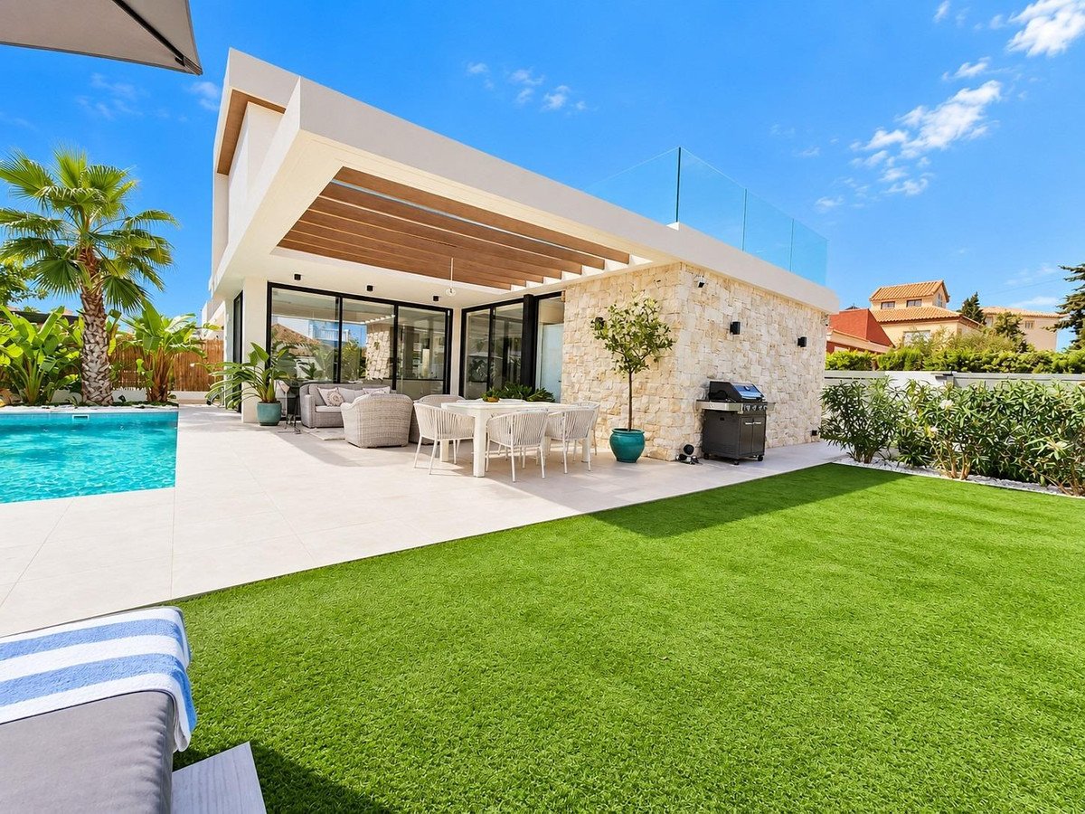 Modern villa with a swimming pool, outdoor dining area, and lush green lawn under a clear blue sky.