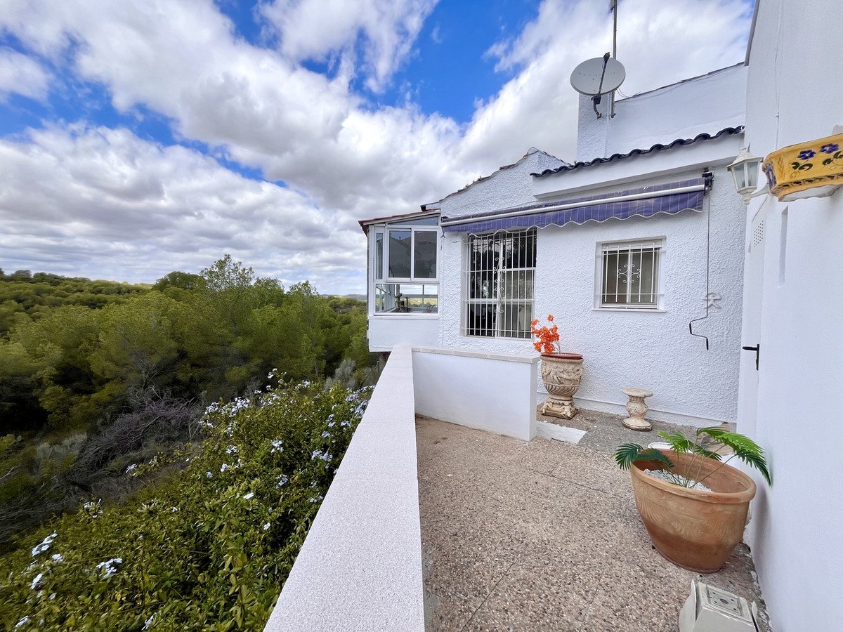 Exterior view of a white house with a terrace overlooking lush green trees and a cloudy sky.