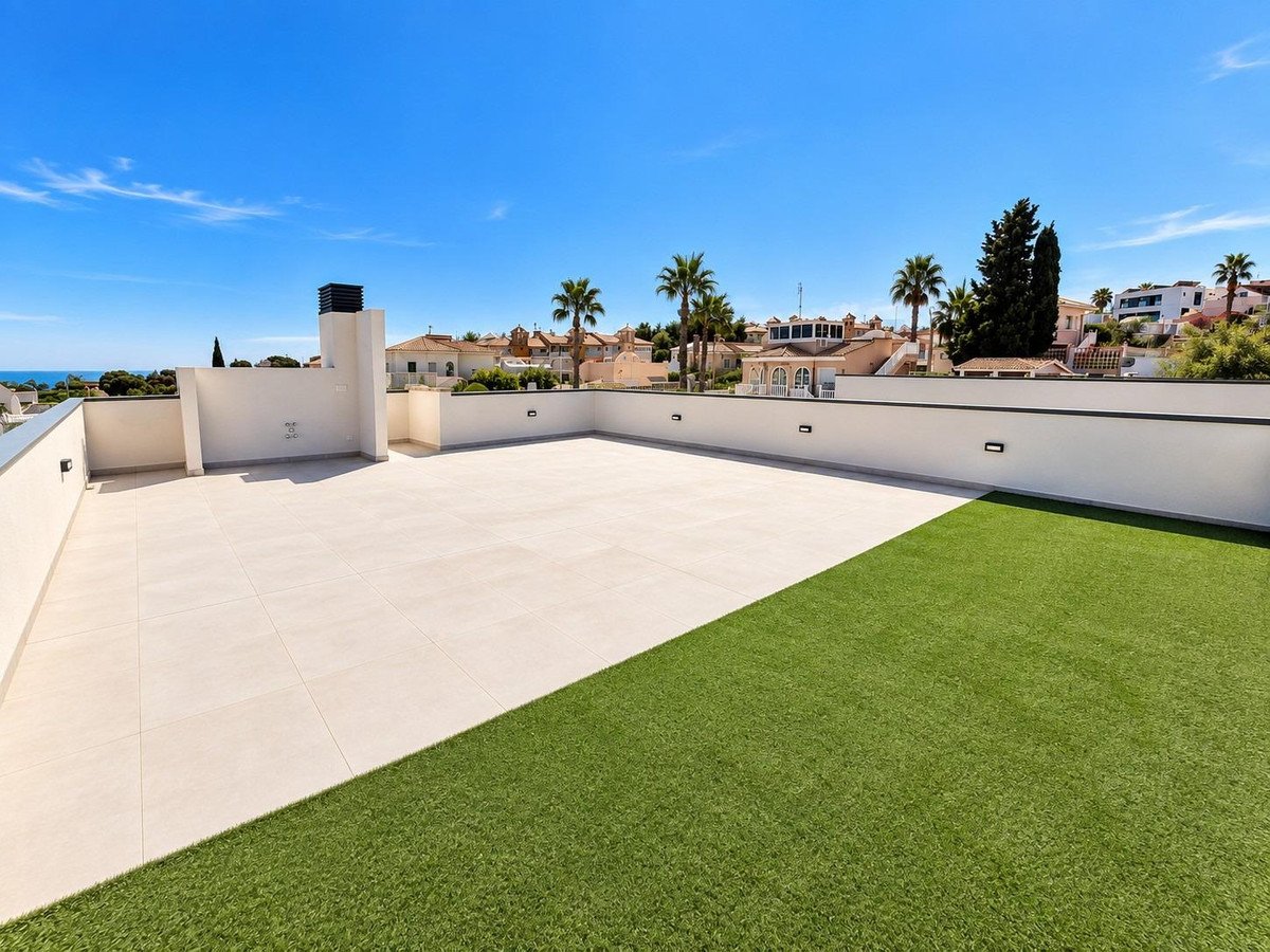 Modern terrace with tiled flooring, artificial turf, and white walls, overlooking a blue sky and distant sea.