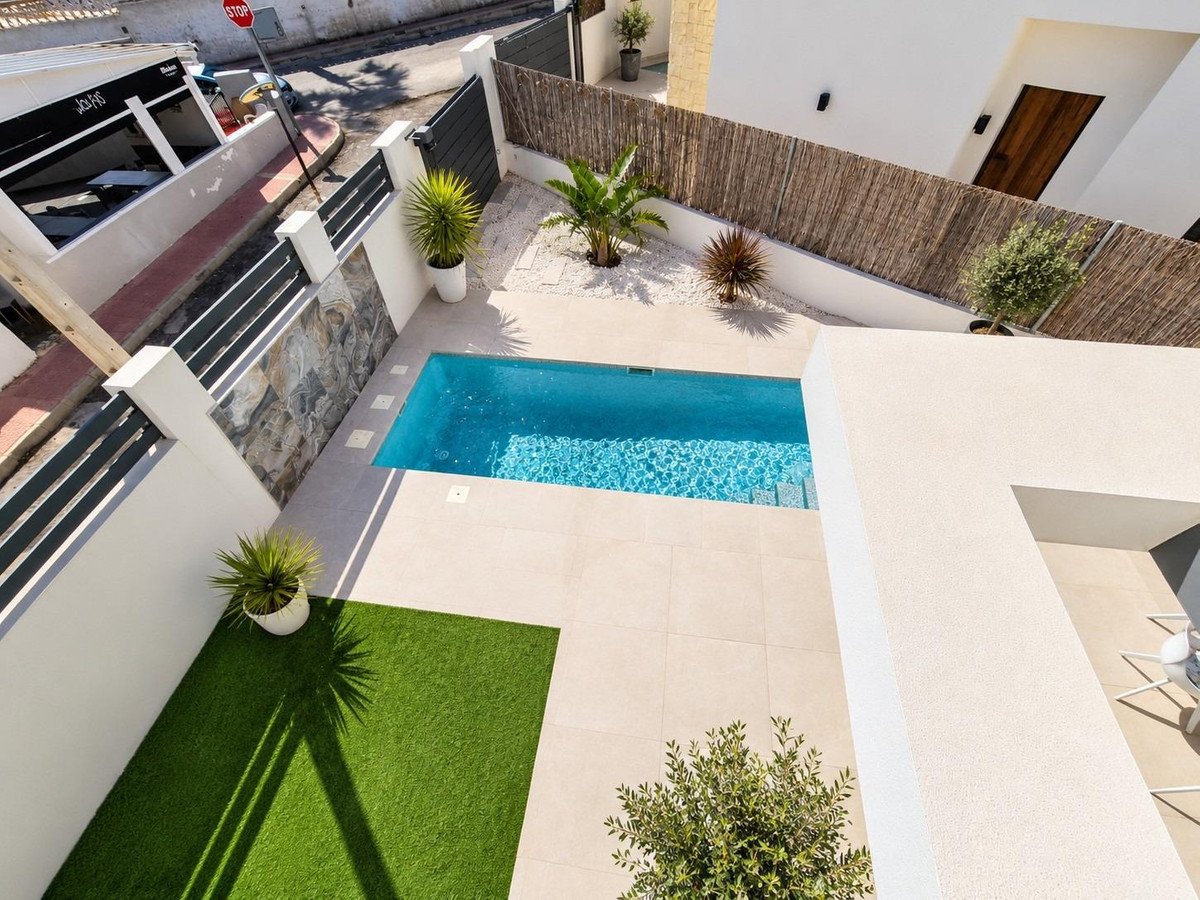 Modern villa outdoor area featuring a sleek swimming pool, artificial turf, and minimalist landscaping under bright sunlight.