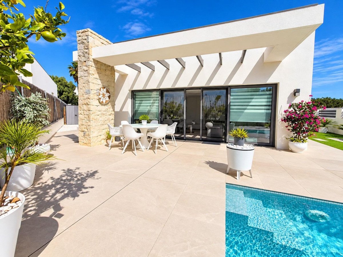Modern villa exterior with a patio, dining set, and a small swimming pool under a bright blue sky.