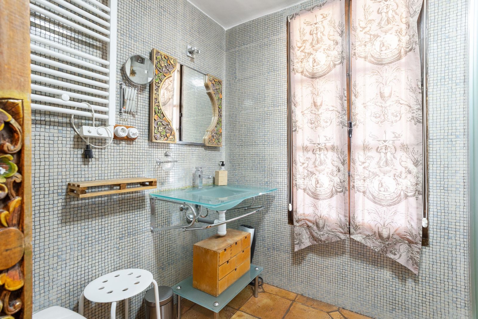 Vintage badkamer met glazen wastafel, mozaïektegels en decoratieve elementen.