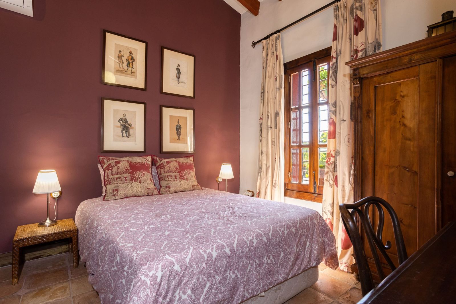 Slaapkamer met antiek meubilair, rode muur en sfeervolle verlichting.