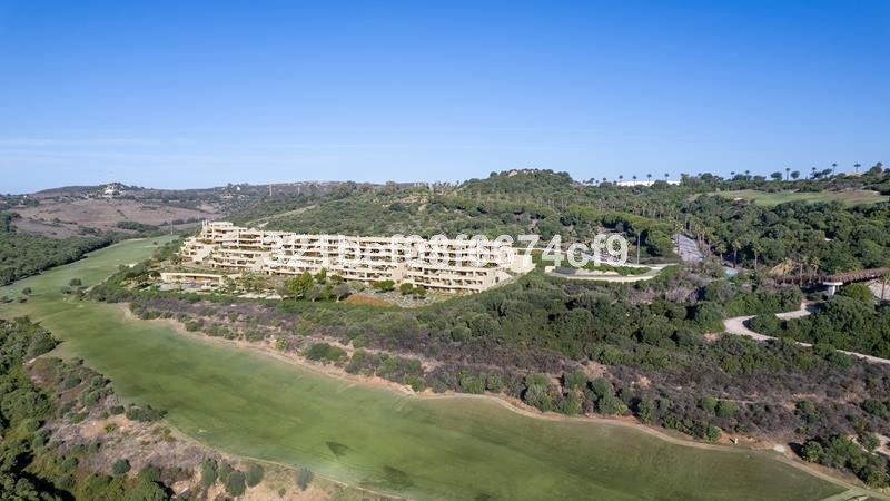 A sprawling modern building complex overlooks a lush green golf course and surrounding hills under a clear blue sky.