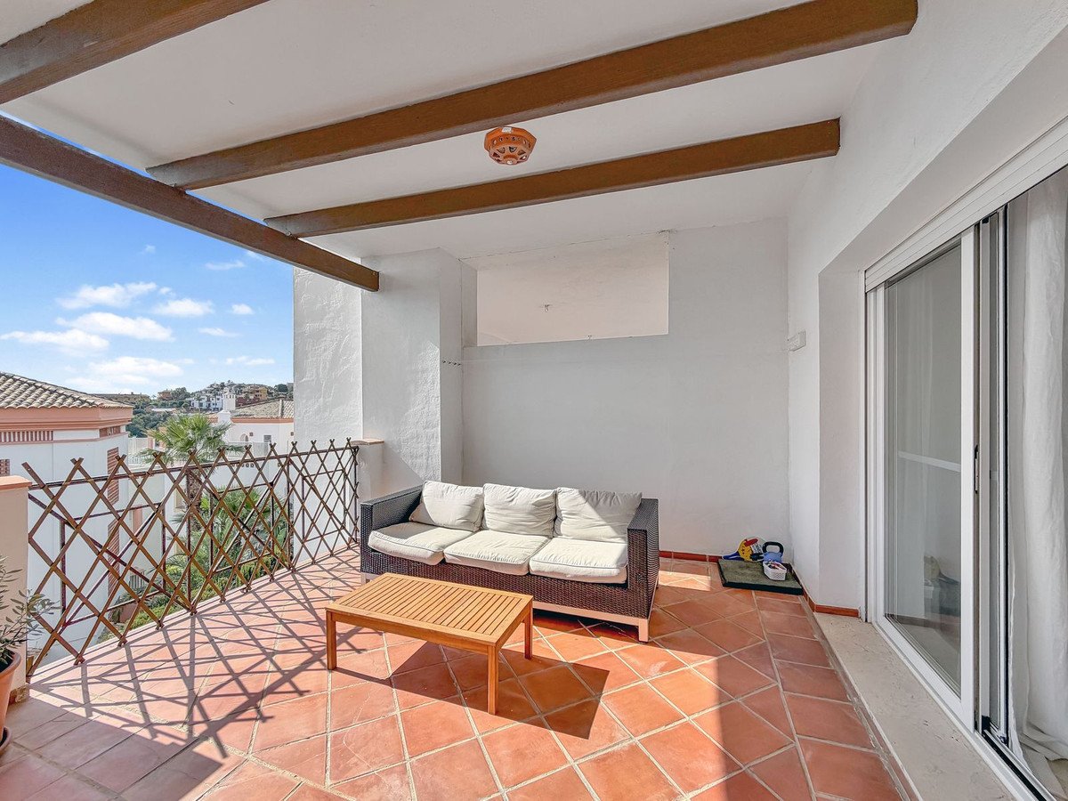 A sunny terrace with a wicker sofa, wooden coffee table, and tiled flooring.
