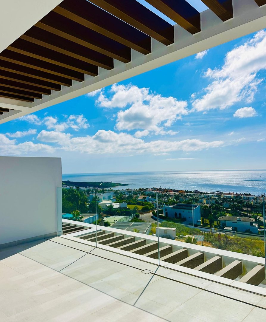 Modern balcony with glass railings offering a stunning sea view of the coast and blue sky with clouds.
