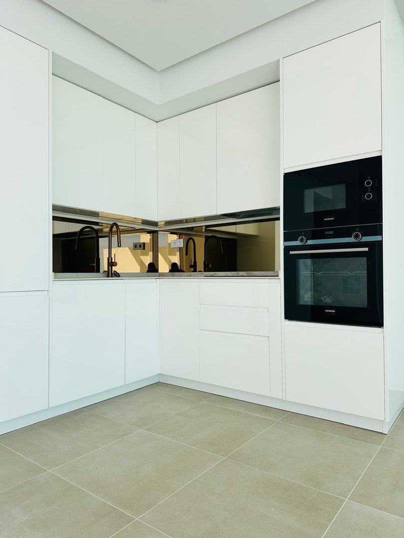 A modern white kitchen with sleek cabinetry, integrated oven, and mirrored backsplash.