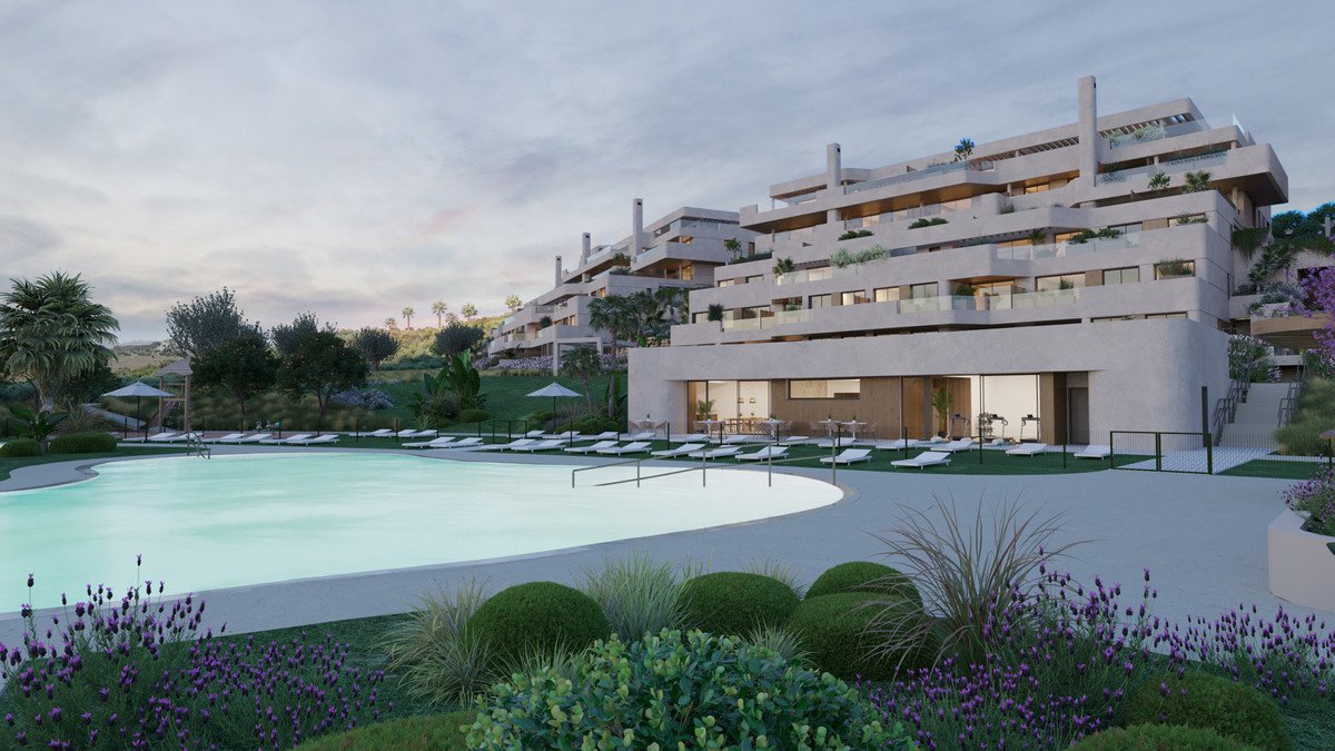 Modern apartment complex with a large swimming pool and lounge chairs, surrounded by landscaped gardens and hills.