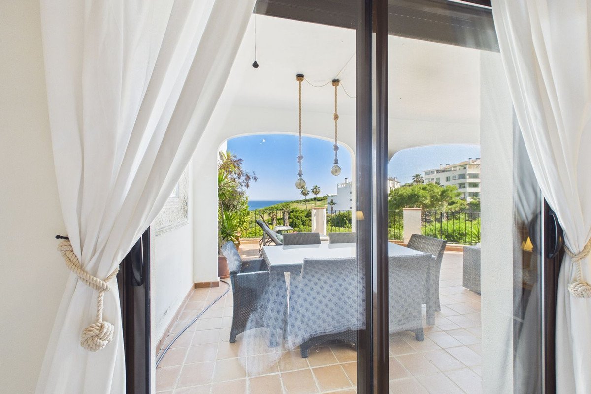Terrace with dining table and chairs, overlooking a lush green landscape and the blue sea.