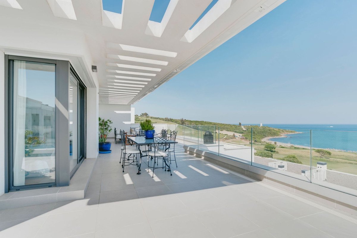 Modern terrace with dining set and glass railings offering a panoramic sea view under a blue sky.