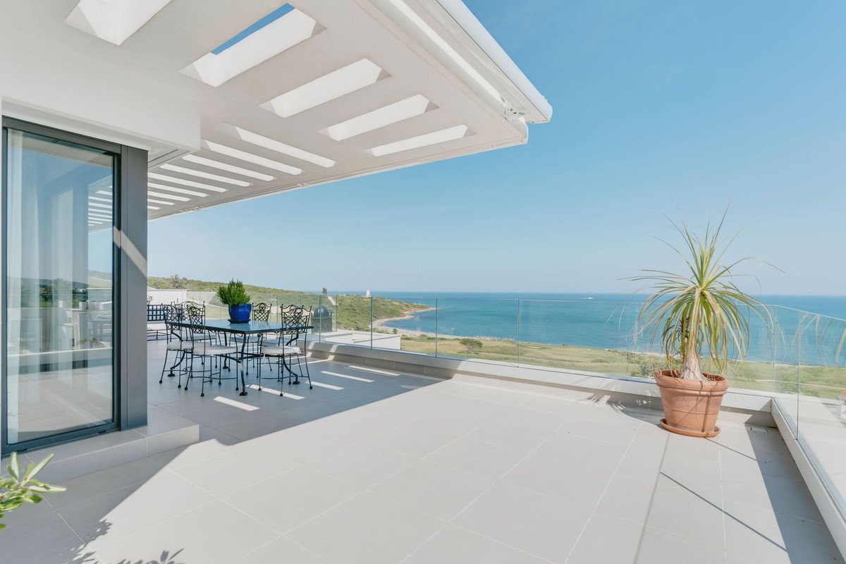 Spacious modern patio with a dining table overlooking a serene ocean and coastline under a clear blue sky.