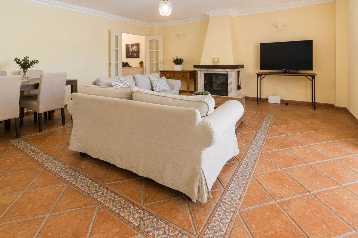 Cozy living room with a beige sofa, fireplace, television, and dining area, featuring terracotta tile flooring and French doors.