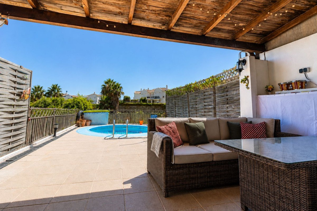 Covered patio with comfortable seating, a glass-top table, and a small blue pool overlooking a residential area.
