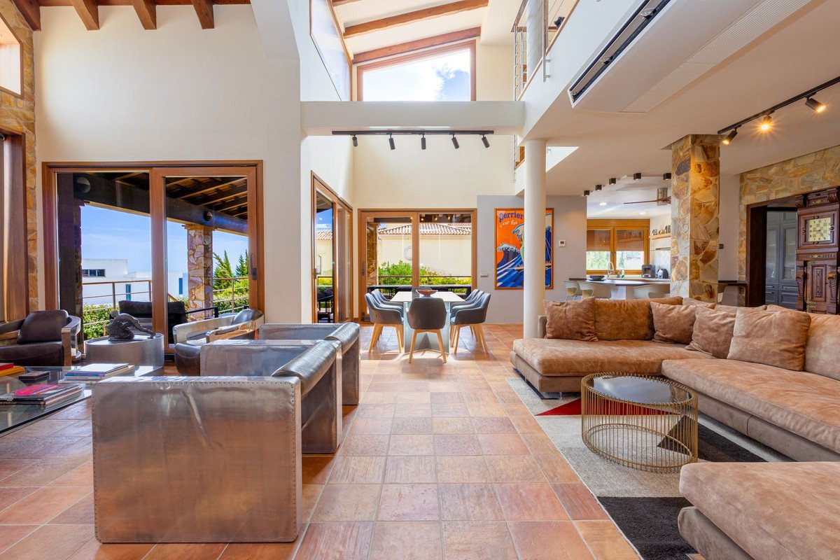 Spacious living and dining area with sea view, modern furniture, and high ceilings with wooden beams.