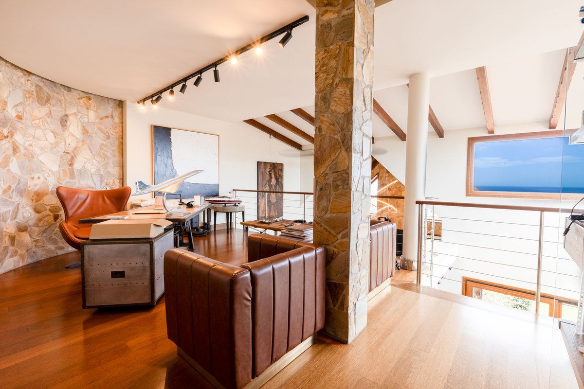 Luxurious office space with leather seating, a desk, and a stunning sea view through a large window.