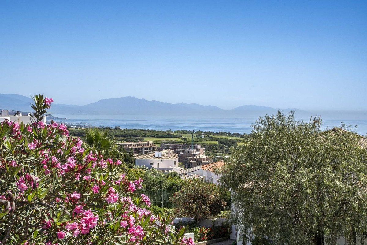 Scenic view of the sea and mountains with pink flowers in the foreground, overlooking a town and golf course.
