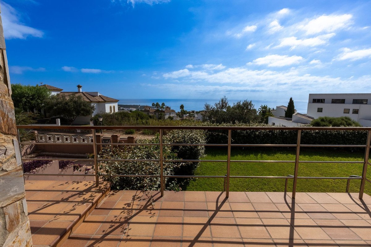 View from a terrace with a sea view, overlooking houses, trees, and a grassy lawn with shadows from the railing.