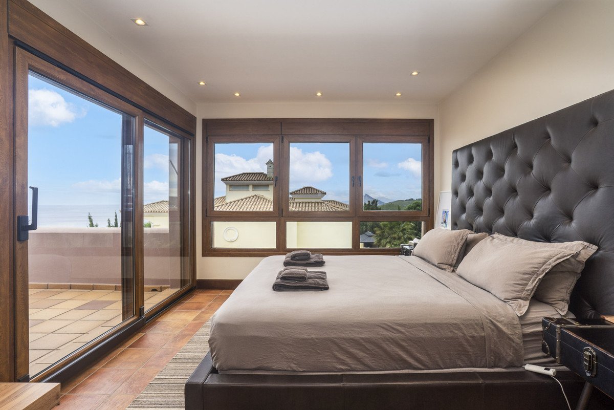 Luxurious bedroom with sea view, balcony access, and large tufted headboard. Features elegant decor.