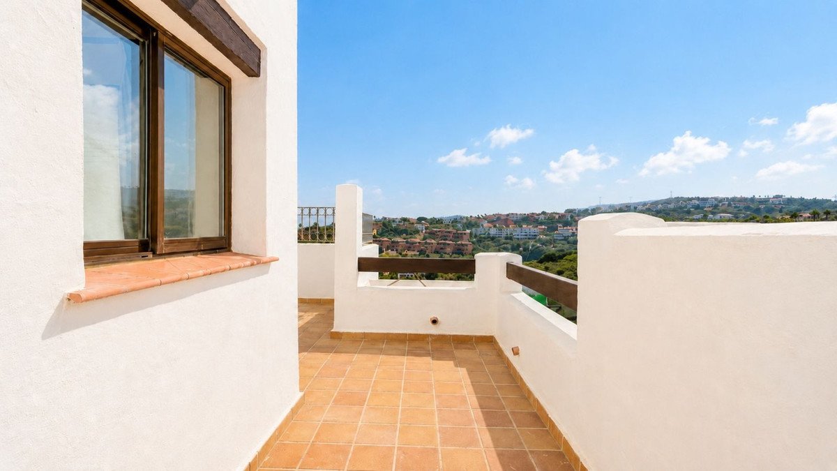 Terrace with tiled floor and white walls, featuring a large window and a view of a town on a hillside.