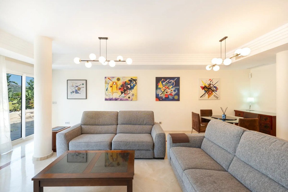 A spacious living room with modern sofas, abstract art on the walls, and large windows offering a view of greenery.