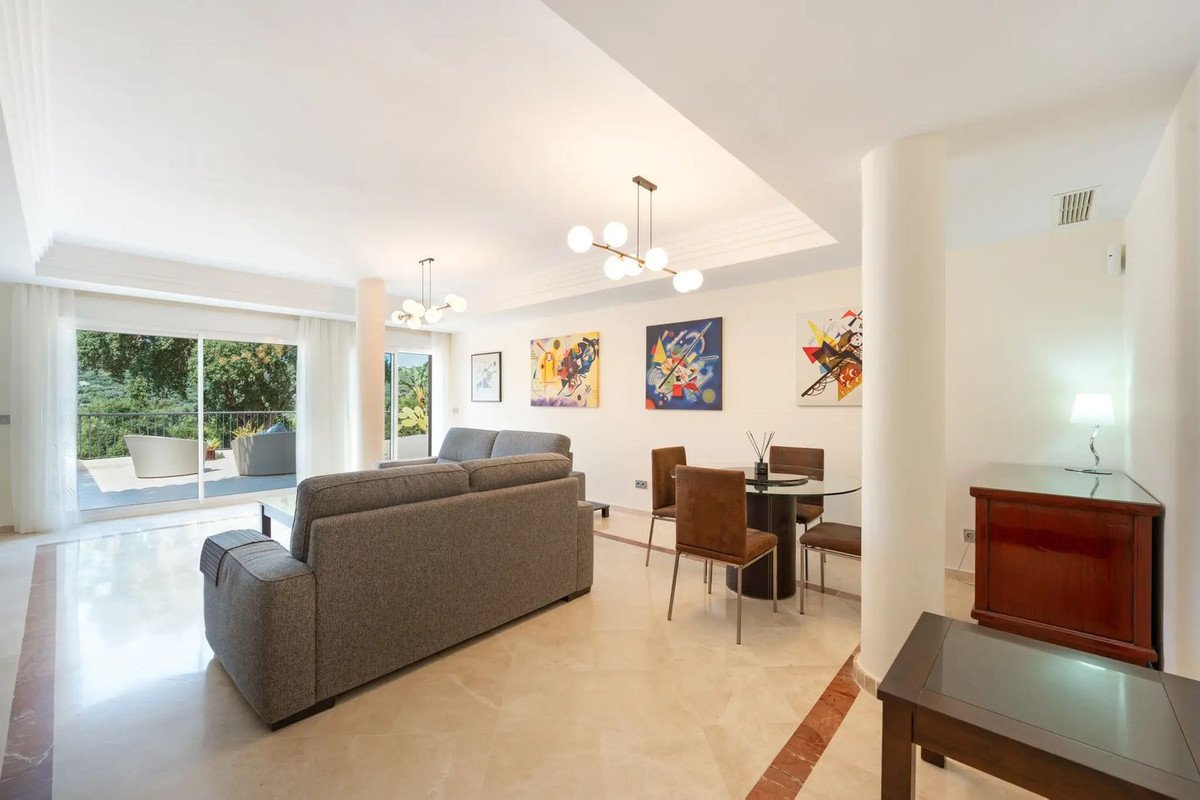 Spacious living and dining area with modern furniture, abstract art, and access to a terrace with a scenic green view.