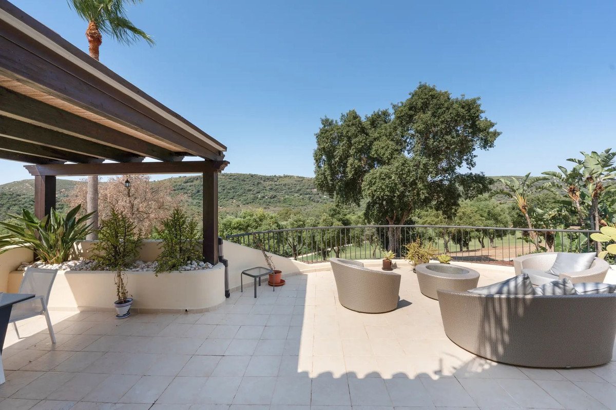 Spacious patio with lounge chairs, under a pergola, overlooking lush green hills and trees.