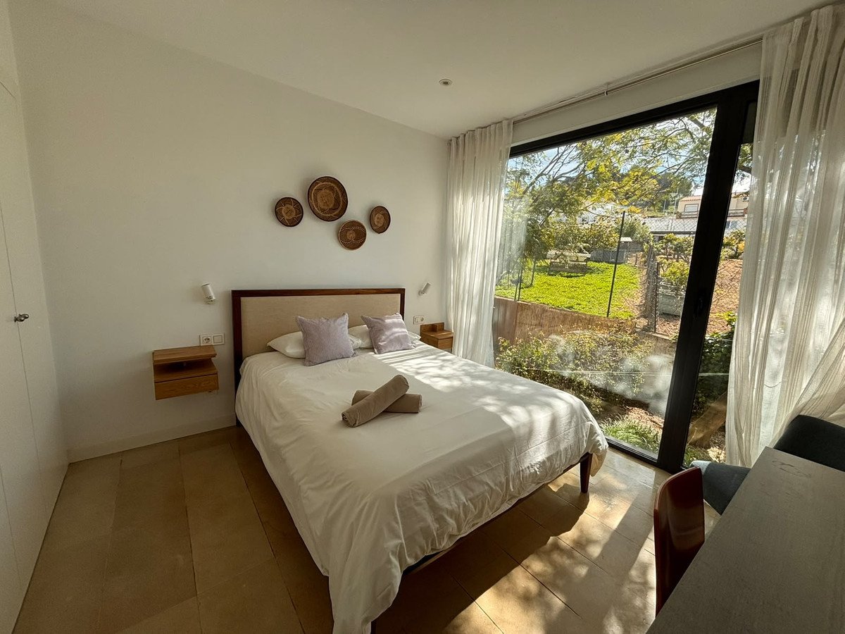 Modern bedroom with a large window overlooking a lush green garden and trees, featuring a comfortable bed and stylish decor.
