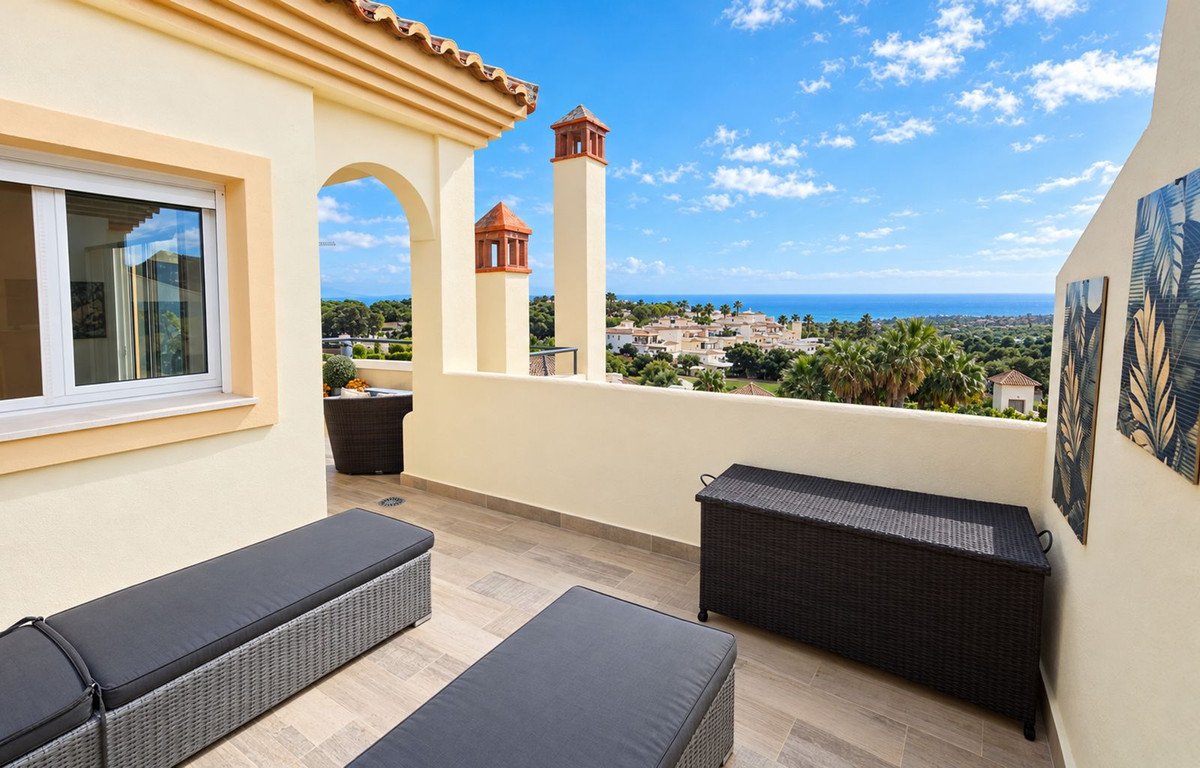 A sunny terrace with outdoor seating overlooking the ocean and coastal town.